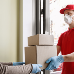 Delivery man wearing a mask and handing over the delivery to the client
